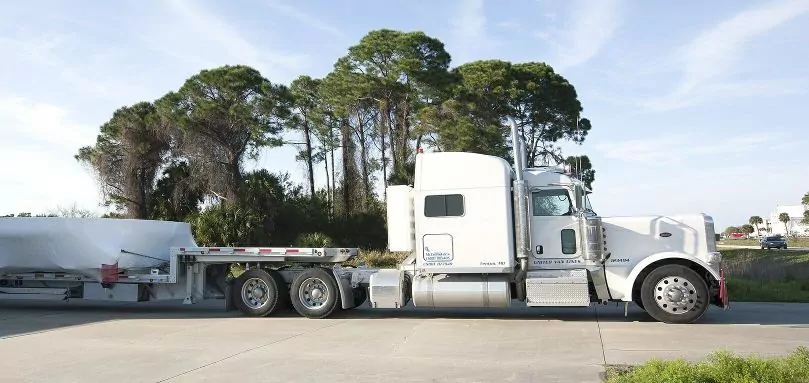 White tractor and step-deck trailer in front of trees