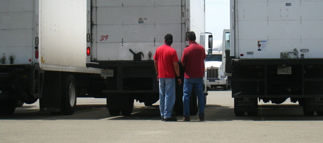 Two men in red t-shirts stand in back of a trailer