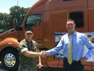 Military man shaking hands with trucking company recruiter in front of orange truck