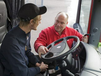 Trainer in red showing truck driver about wheel